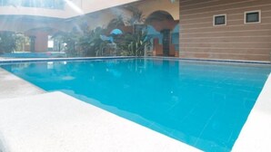 Una piscina con superficie de agua azul cristalina, rodeada por un edificio con fachada de azulejos y un balcón con vistas a la piscina.