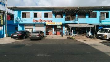 Un edificio comercial con letrero de RedDoorz, varios autos estacionados y un área exterior techada.