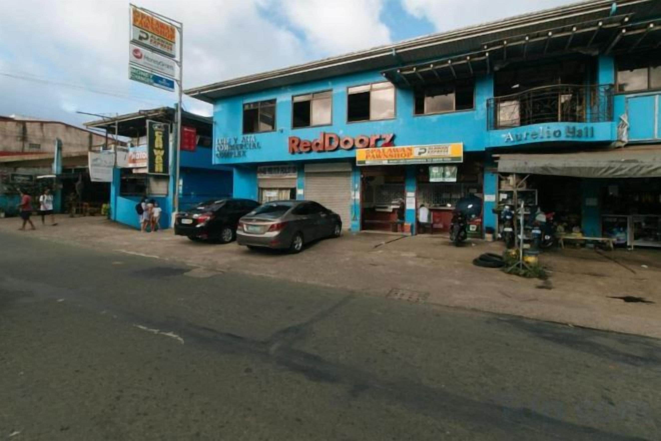 Um edifício com a placa RedDoorz, uma motocicleta estacionada na frente e uma placa de sinalização à esquerda.