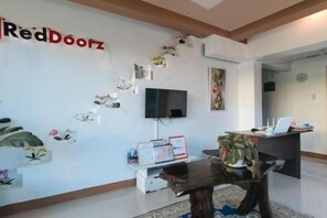 Zona de recepción con televisor de pantalla plana, escritorio y una mesa de centro.