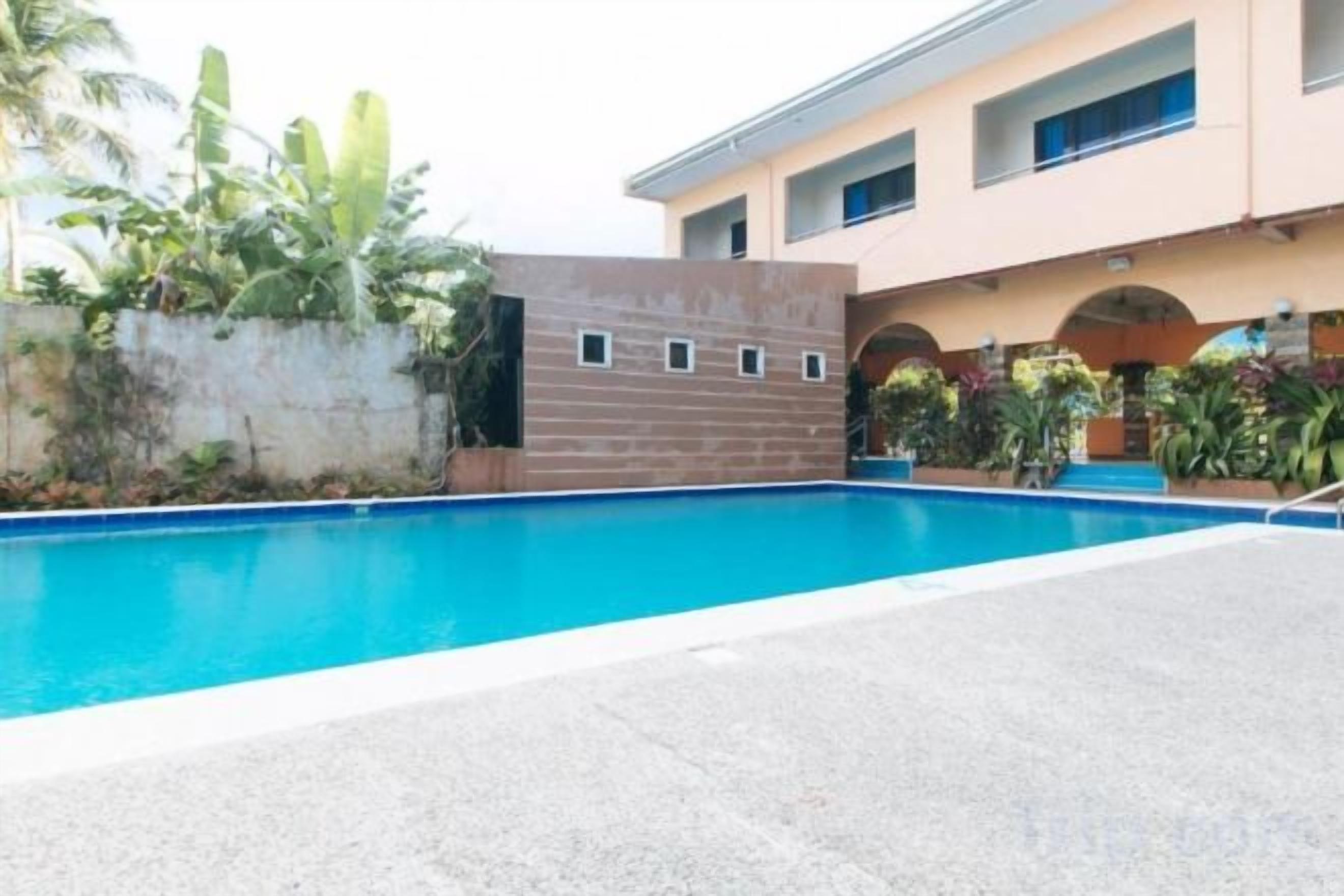A swimming pool with a concrete deck, a brick wall, and a building with multiple windows and arches.