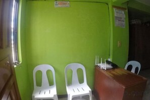Una habitación con una pared verde, dos sillas de plástico blancas, un escritorio de madera y una silla blanca.