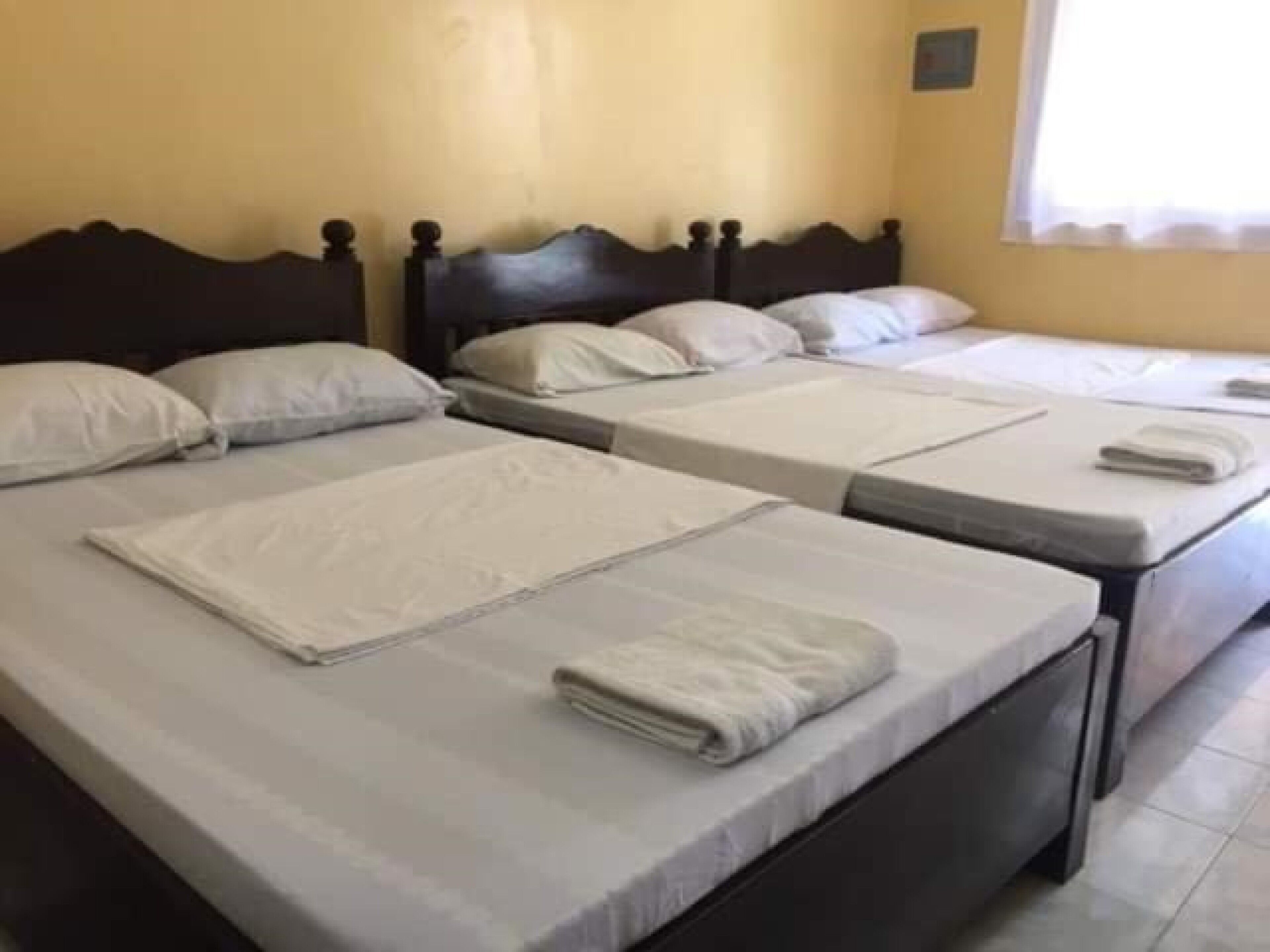 Ein Hotelzimmer mit drei Einzelbetten, jeweils mit ordentlich bezogenem Bettzeug und Kissen.