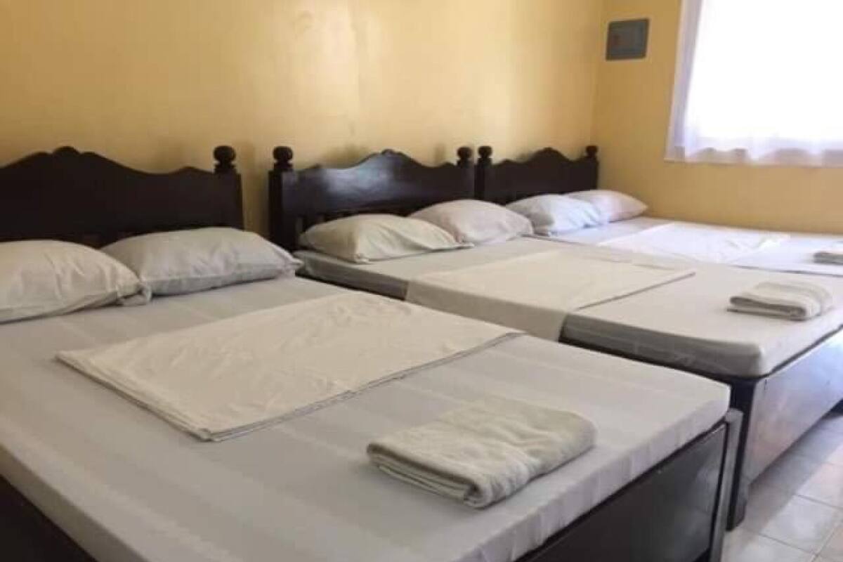A hotel room with three single beds, each with a neatly made bedspread and pillows.