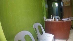 Una habitación con una pared verde, un escritorio de madera y dos sillas de plástico blancas.