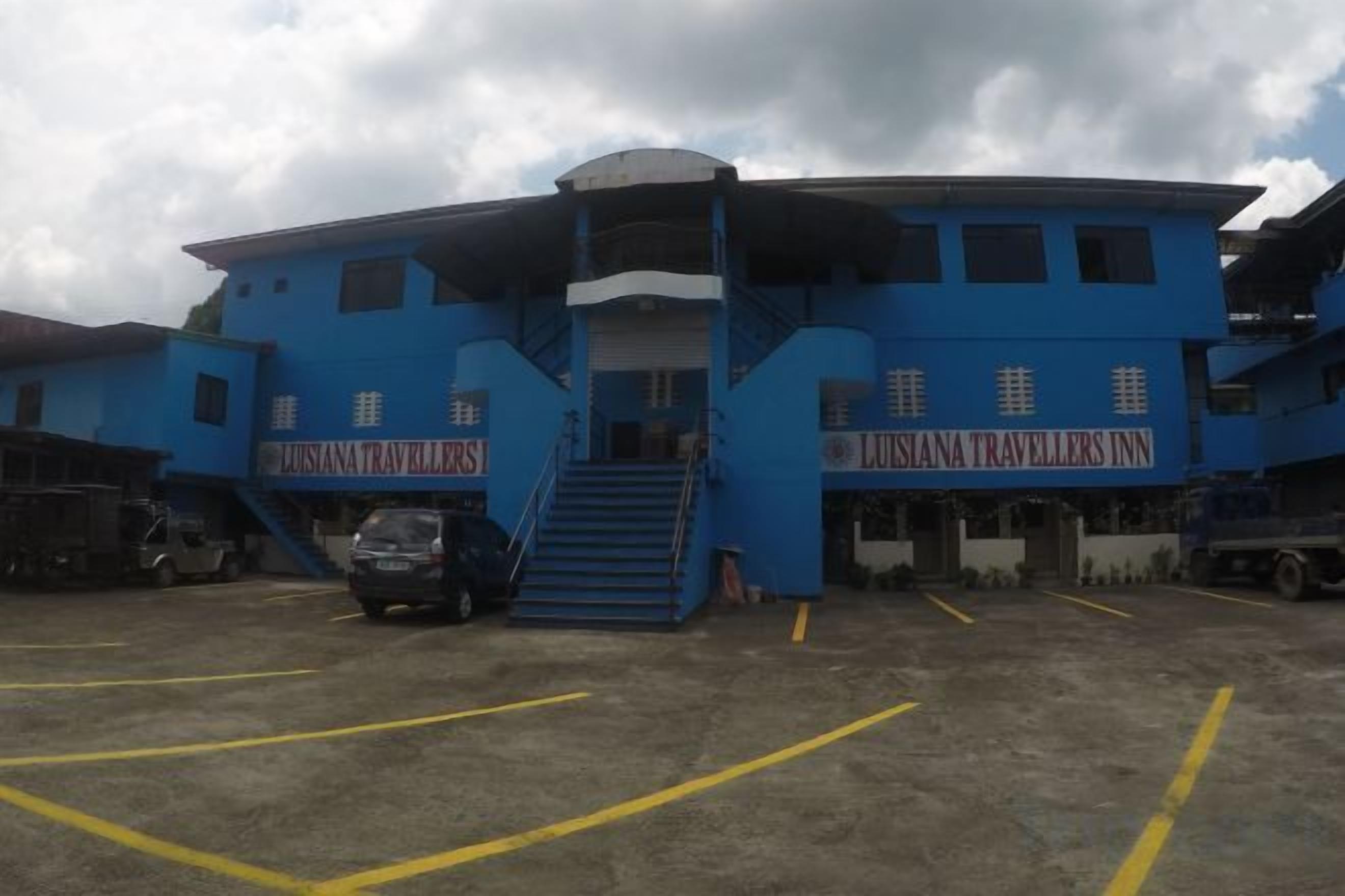 A blue building with 'LUSIANA TRAVELLERS INN' signage, a staircase, and a parking lot.