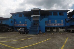Un edificio azul con letrero 'LUSIANA TRAVELLERS INN', una escalera y un estacionamiento.