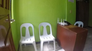 A room with green walls, a wooden door, two white plastic chairs, a small desk with a telephone and a router, and a calendar on the wall. - Reddoorz Plus Near Municipality of Luisiana Laguna (Luisiana)