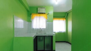 Una cocina pequeña y estrecha con paredes verdes, una encimera blanca y una ventana con cortinas amarillas.