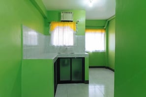 Una cocina pequeña y estrecha con paredes verdes, una encimera blanca y una ventana con cortinas amarillas.