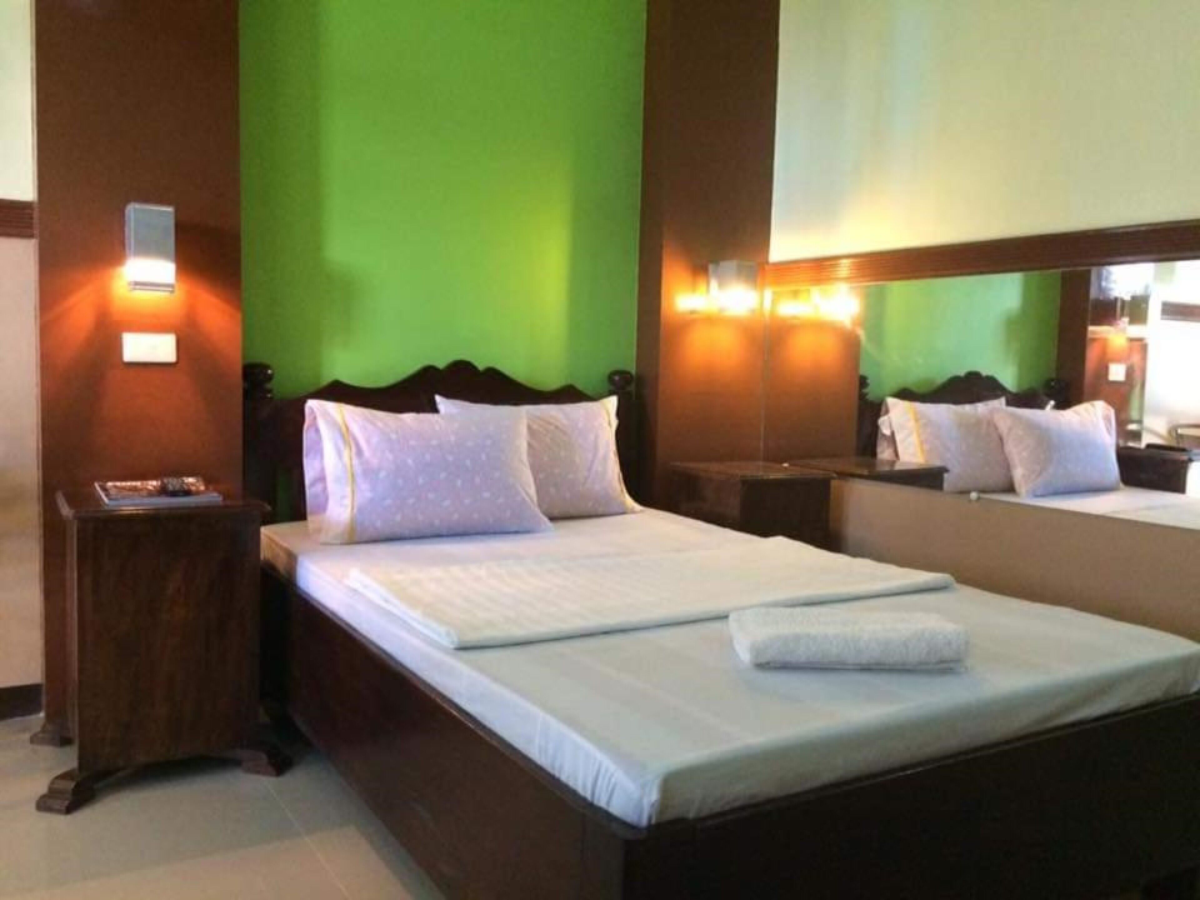 Ein Hotelzimmer mit einem großen Bett, einem Nachttisch, einem Spiegel und grünen Wänden.