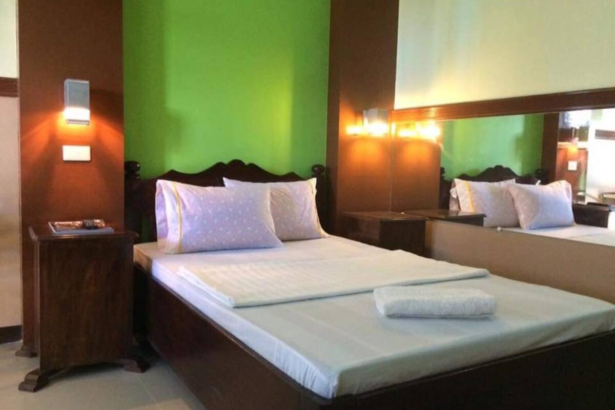A hotel room with a large bed, a nightstand, a mirror, and green walls.