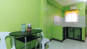 Una cocina pequeña con una pared verde, una mesa blanca y una silla blanca. Hay dos botellas sobre la mesa.