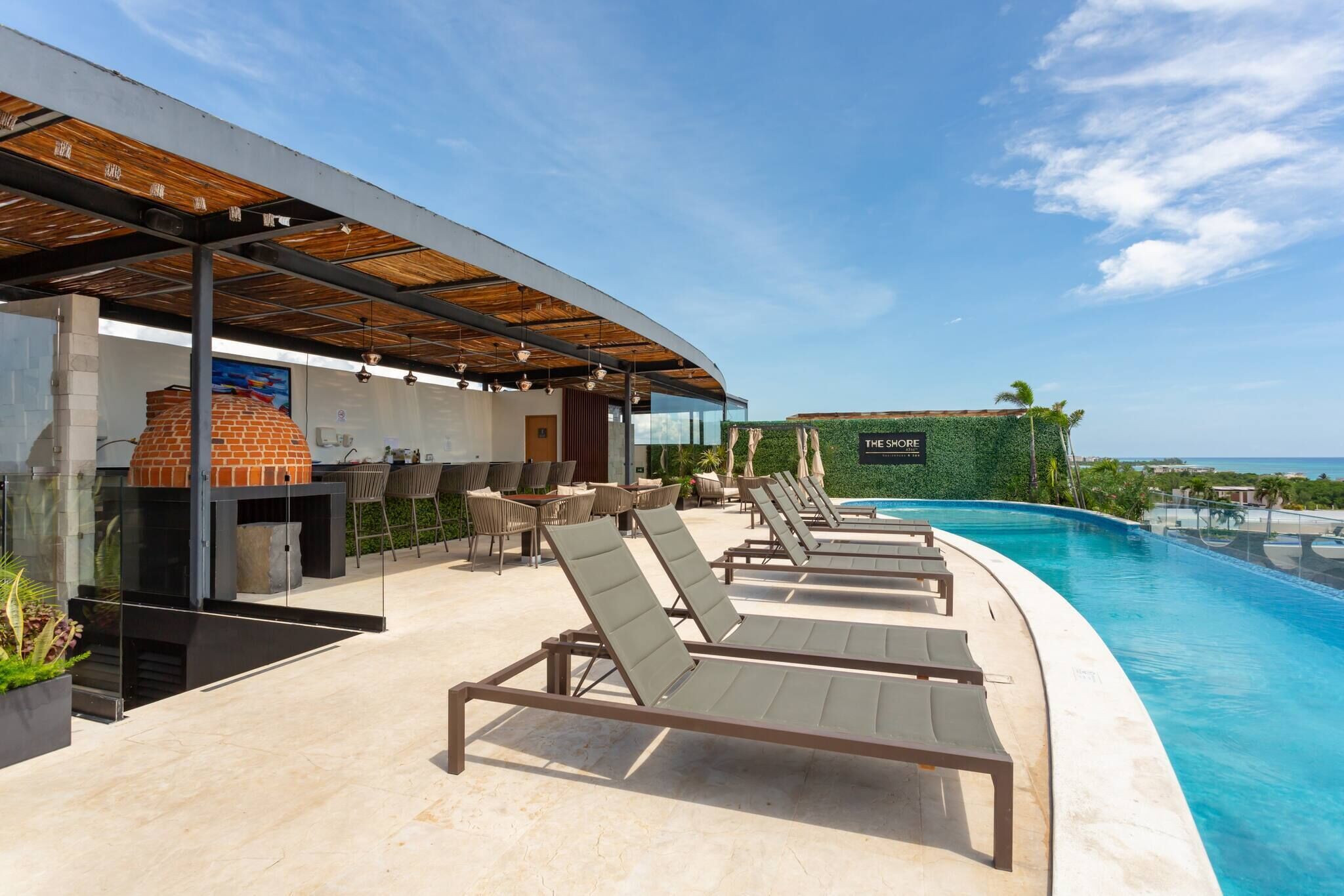 A poolside area with lounge chairs, a barbecue, and a view of the ocean.