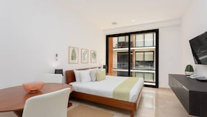 A modern hotel room with a wooden bed, a desk, a chair, a TV, and a large window with a view of the city. - Cozy Studio In Playa Del Carmen Downtown - Few Steps From the Beach!!! (Playa del Carmen)