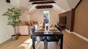 Une pièce aménagée dans les combles, avec une table à manger pour quatre personnes, un canapé, un téléviseur et une grande fenêtre.