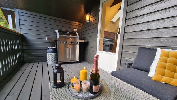 Une terrasse en bois avec un barbecue, une bouteille de champagne, des bougies et une lanterne.