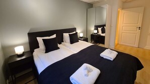 Un lit bien fait, avec une literie noire et blanche, une table de chevet avec une lampe et un miroir accroché au mur.