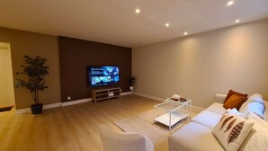 Un salon moderne avec un téléviseur à écran plat, un canapé blanc, une table basse et une plante en pot.