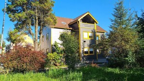 Une maison à deux étages avec un balcon, entourée d’arbres et d’herbe.