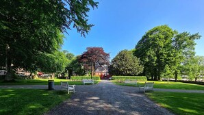 Un chemin de gravier mène à un bâtiment rouge, bordé d’une clôture blanche, dans un parc.