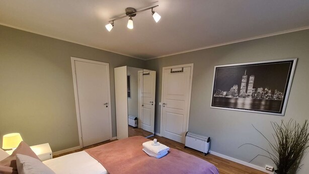 Een slaapkamer met een bed, een nachtkastje, een heater, een spiegel en een poster van een stadsgezicht aan de muur.