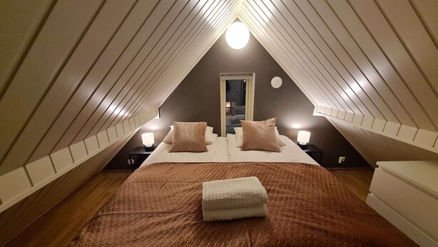 A cozy attic bedroom with a large bed, two bedside lamps, and a window.