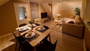 A cozy living room with a dining area, a TV, and a staircase.