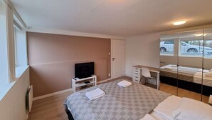 Een slaapkamer met een bed, bureau, televisie en spiegel.