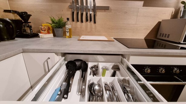Een keuken met een lade-organizer met keukengerei, een koffiezetapparaat en een plant op het aanrecht.