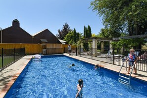 Et rektangulært swimmingpool med en træterrasse og et sort metalhegn.