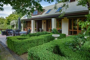 A house with a covered patio, outdoor seating, and a well-maintained garden. - Manata Homestead and Lodge (Otago)