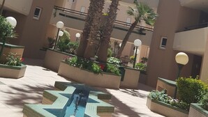 Une cour intérieure avec une piscine centrale, entourée de palmiers et de jardinières.