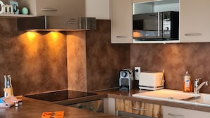 Une cuisine moderne dotée d’un îlot central, d’appareils électroménagers en acier inoxydable et d’un four à micro-ondes placé au-dessus du plan de travail.