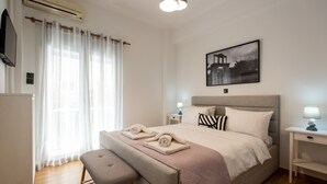 Un dormitorio moderno con cama, mesitas de noche, un banco y una ventana con cortinas.