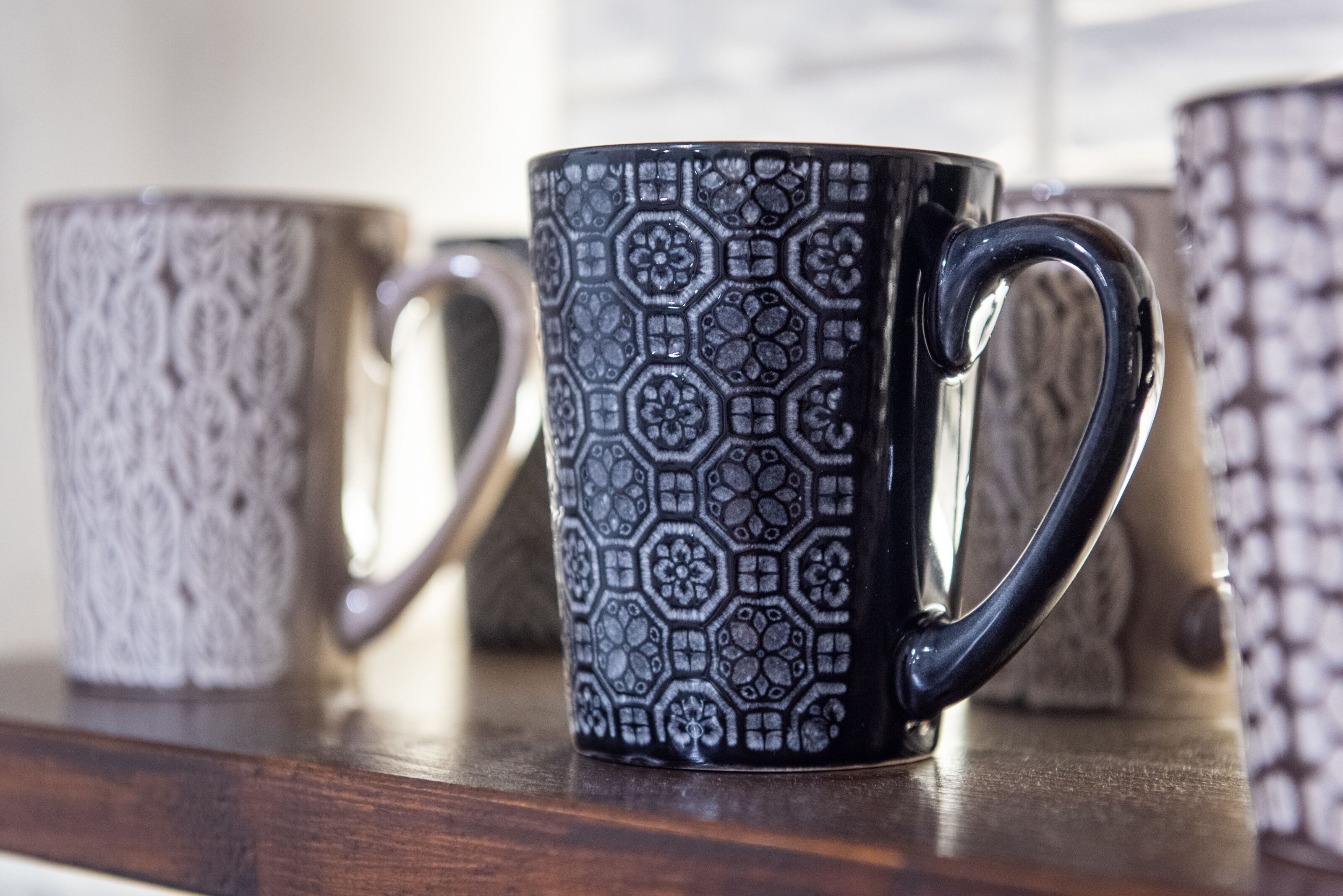 Une rangée de tasses en céramique ornées de motifs complexes, posées sur une surface en bois.