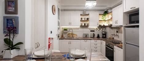 Une cuisine moderne avec des meubles blancs, des appareils en acier inoxydable et une table à manger en bois pour quatre personnes.