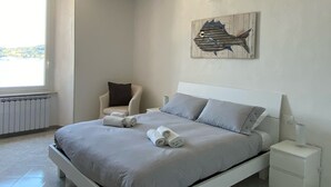 Une chambre à coucher comprenant un lit, une chaise, une table de chevet et une œuvre d’art accrochée au mur.