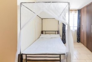 Comfortable bed with a mosquito net canopy, situated against a wall with a nearby wardrobe.
