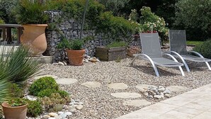 Un patio con plantas en macetas, un muro de piedra y una zona de estar con sillas.