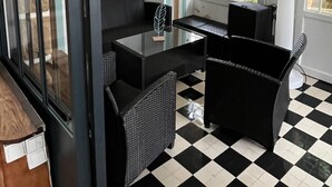 Una habitación con piso a cuadros, muebles negros y blancos, una lámpara blanca y una ventana con vista a follaje.