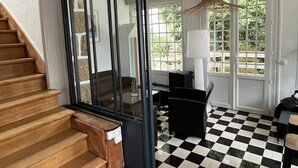 Una escalera conduce a una habitación con piso a cuadros blanco y negro, una silla negra y una mesa con una lámpara.