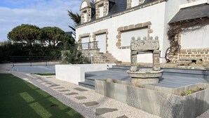 Un patio con una fuente de piedra, un edificio blanco con detalles de piedra y un césped verde.