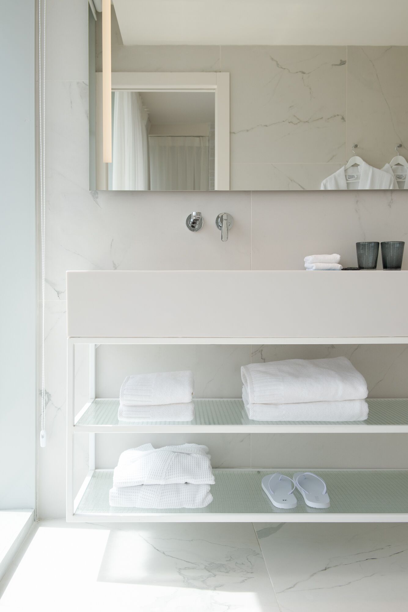 Une salle de bain moderne avec un meuble-lavabo blanc, un pare-feu en marbre et un grand miroir.