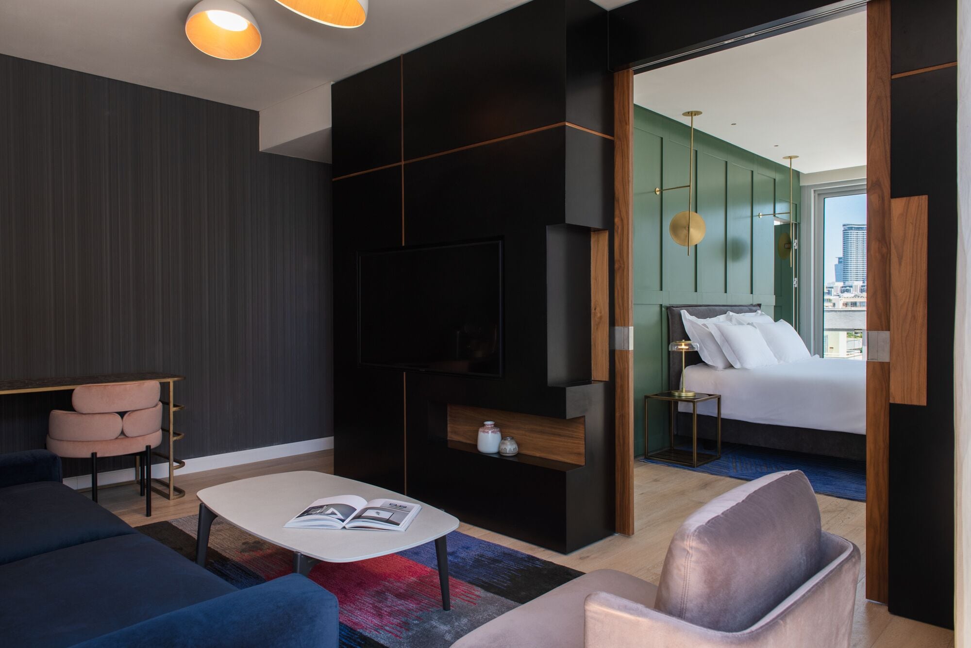 Una habitación de hotel moderna con un panel de madera oscura, una cama grande con ropa de cama blanca, una mesita de noche con una lámpara, un sofá y una mesa de centro con una revista.