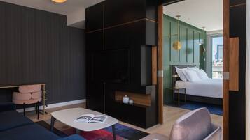 Una habitación de hotel moderna con un panel de madera oscura, una cama grande con ropa de cama blanca, una mesita de noche con una lámpara, un sofá y una mesa de centro con una revista.