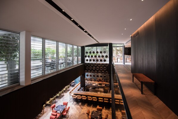 A modern bar area with a high ceiling, large windows, and a variety of seating options.