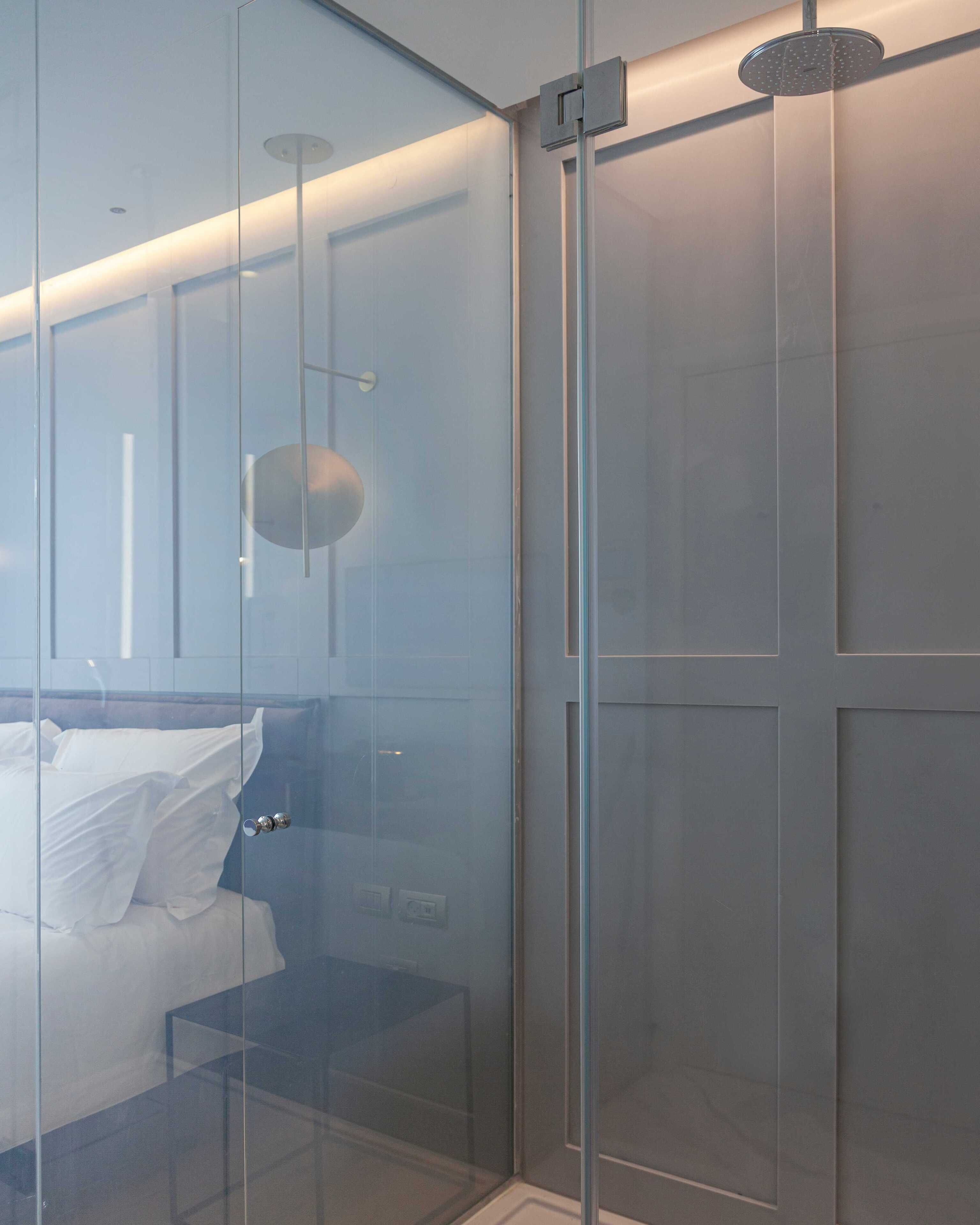 A modern bathroom with a glass shower enclosure, a visible showerhead, and a bed with white linens.