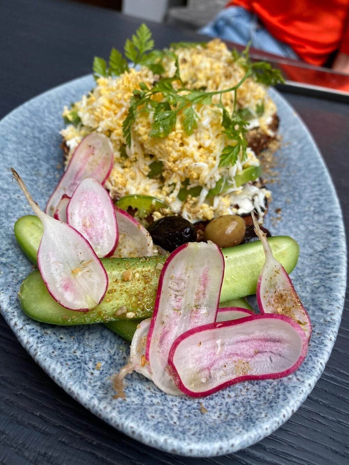 A plate with a salad consisting of cucumbers, radishes, and a grainy topping, possibly quinoa or couscous, garnished with parsley.