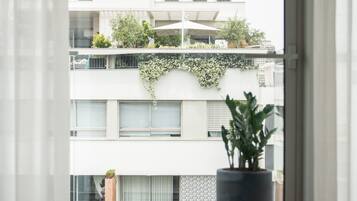 Un apartamento moderno con un amplio ventanal, una planta en maceta y vistas de edificios vecinos.